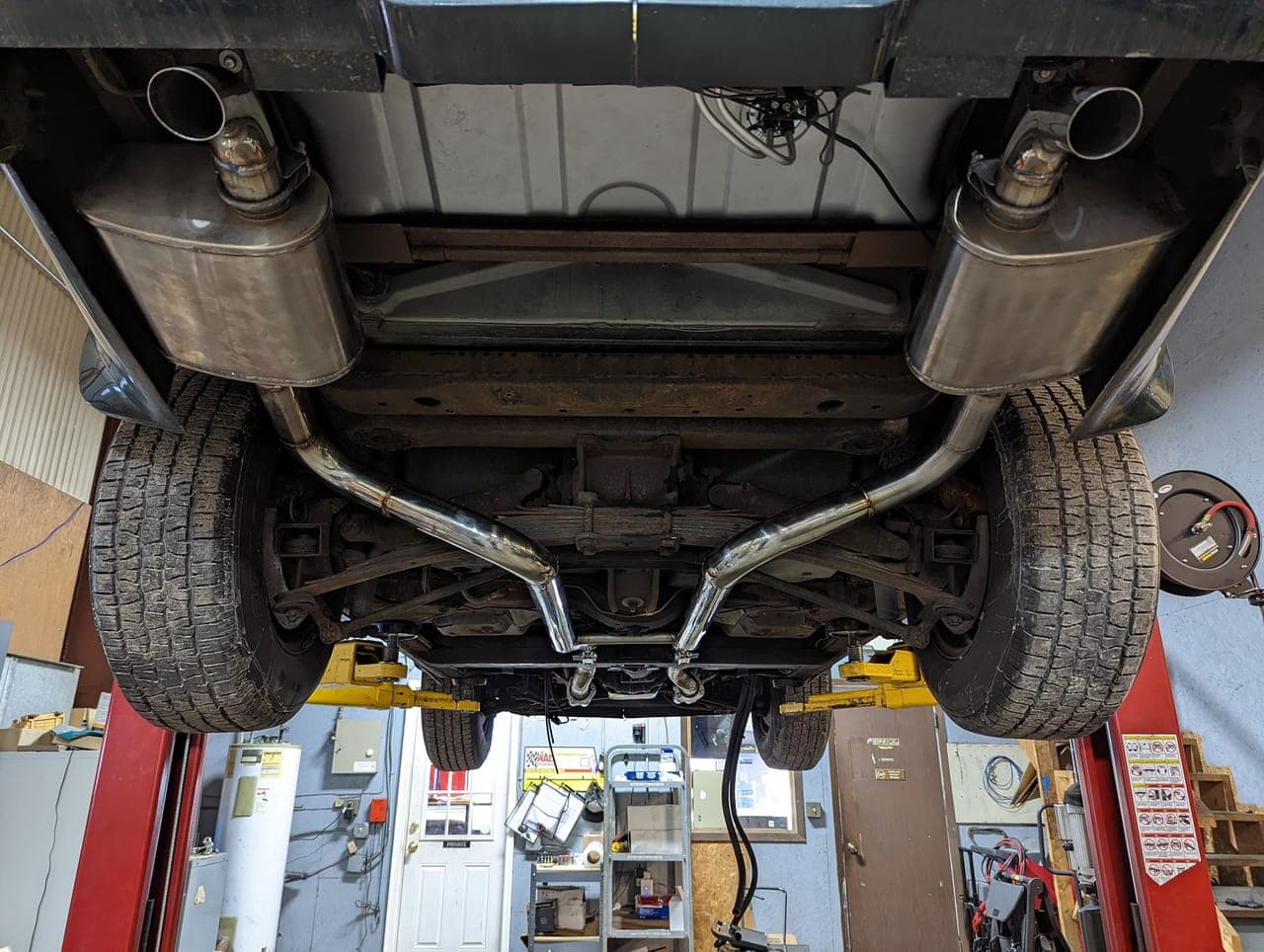 Underside of the 1974 Corvette on a lift showing a polished dual exhaust system, mufflers, driveshaft, and rear suspension