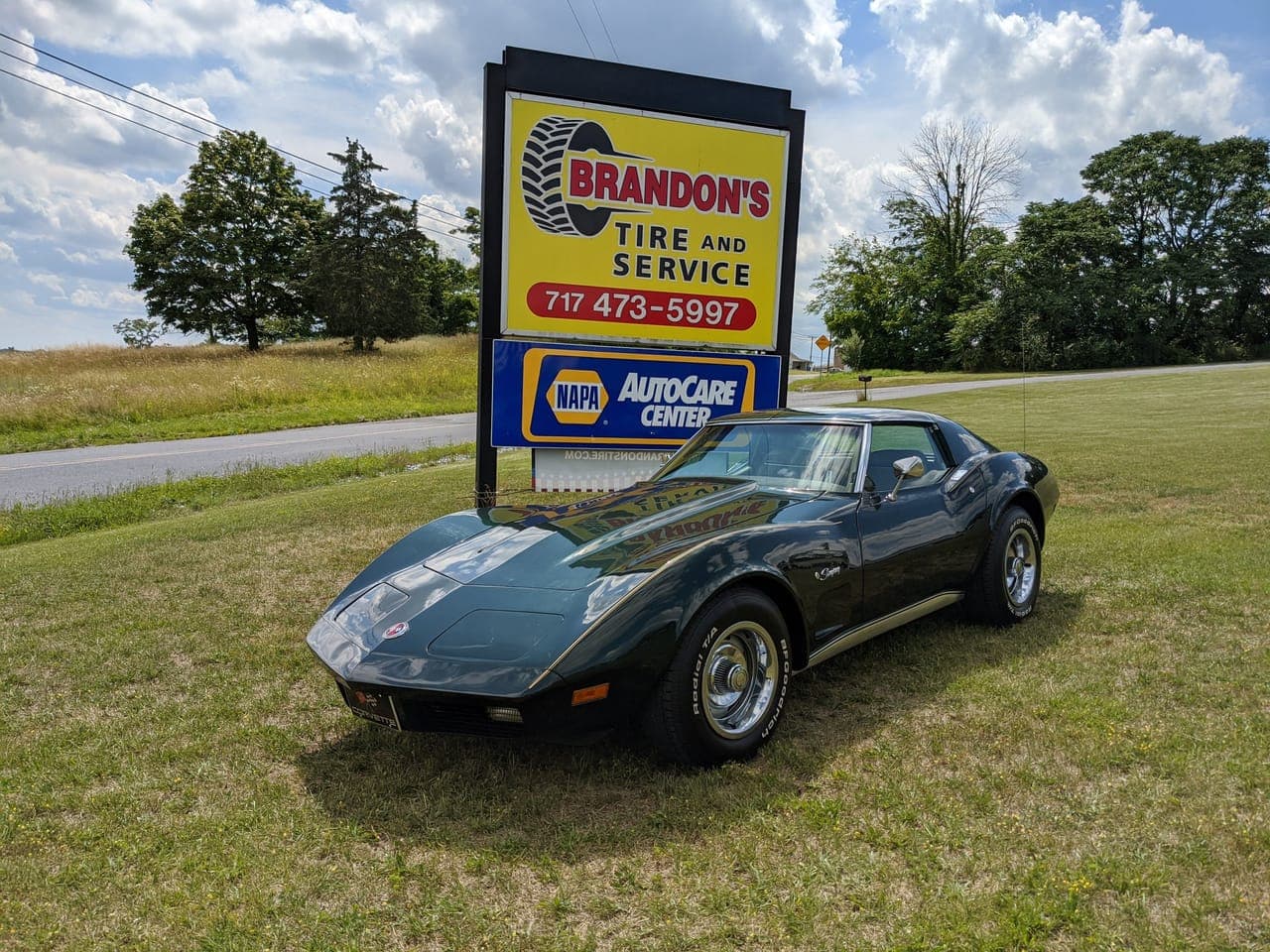 Dark green 1974 Corvette parked beside the Brandon's Tire and Service road sign with the NAPA AutoCare logo