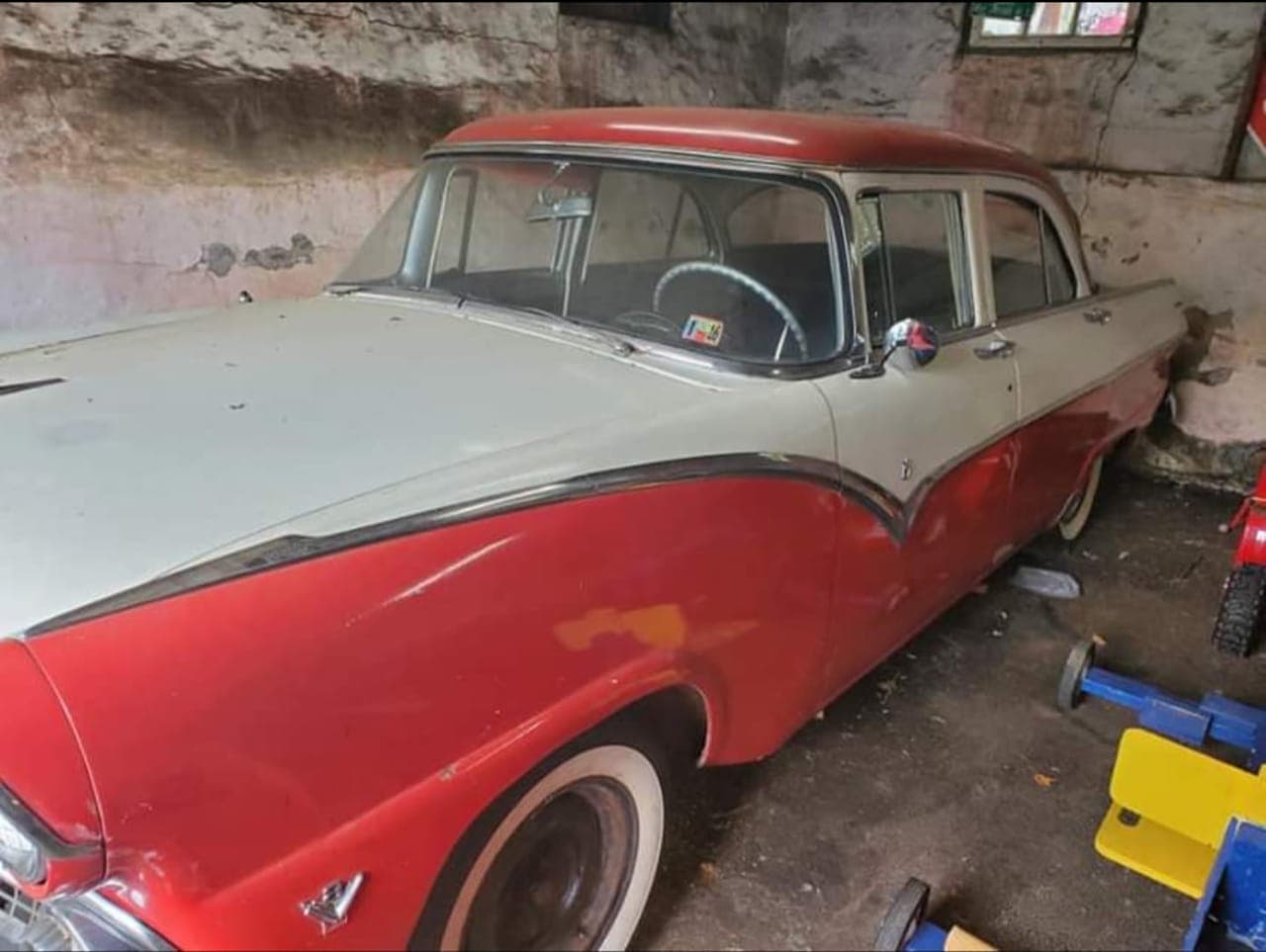 Side view of the dusty red-and-white 1955 Ford Fairlane before restoration, showing faded paint and surface rust