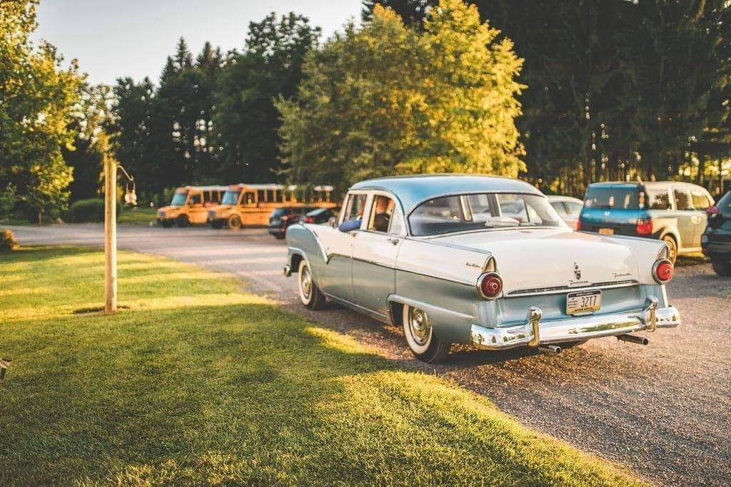 Rear three-quarter view of the restored blue-and-white 1955 Ford Fairlane parked outdoors at golden hour