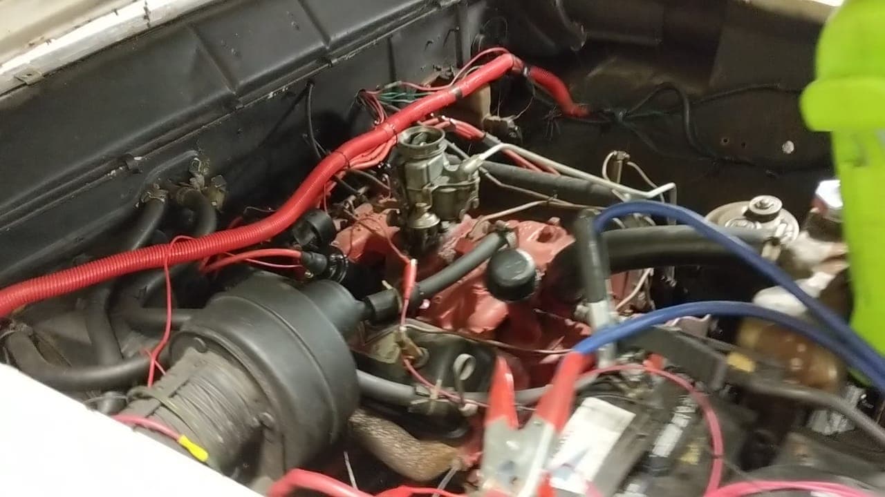 Engine bay of the 1955 Ford Fairlane with the freshly detailed red Y-block V8 running for the first time, jumper cables clipped to the battery