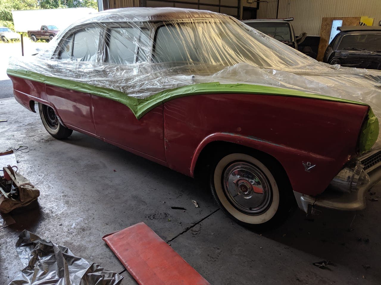 Red 1955 Ford Fairlane masked off with plastic sheeting and green tape in the shop bay, ready for paint