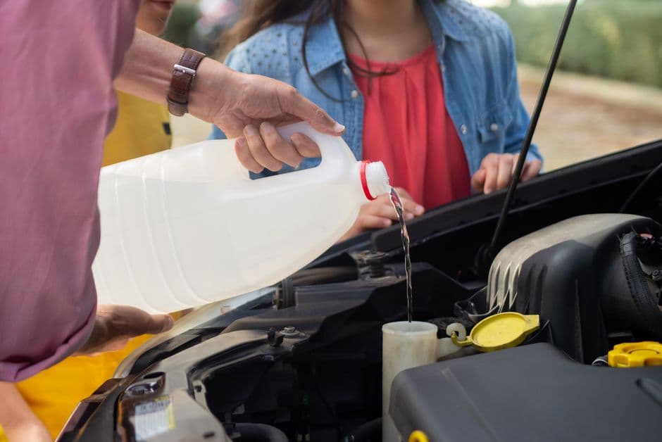 Close-up of a person pouring windshield washer fluid into a car before summer driving in Pennsylvania.