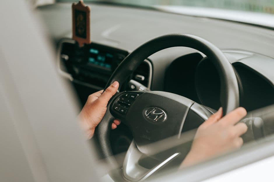 Close-up view of hands holding a slightly off-center steering wheel inside a car.