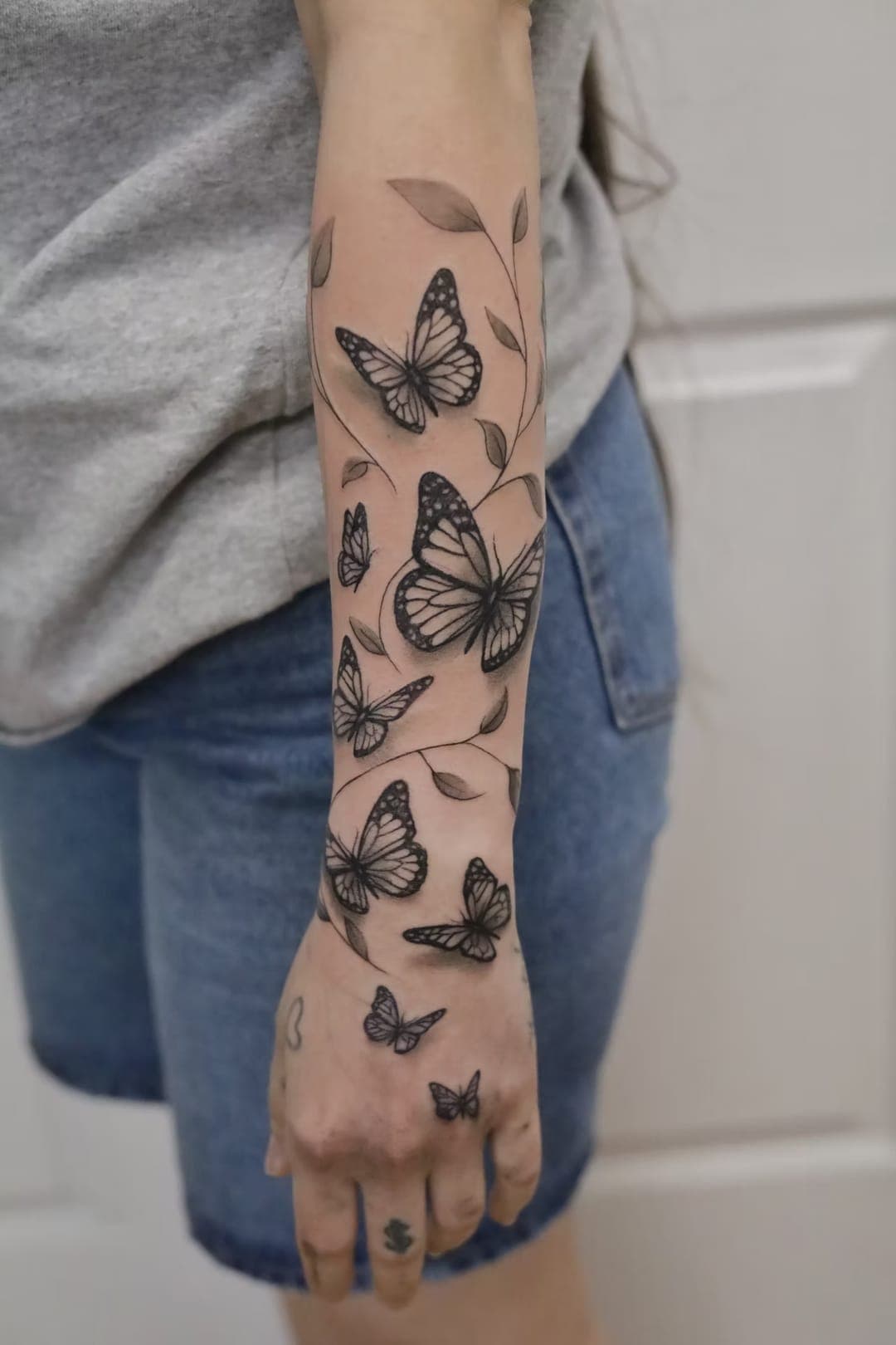 Black-and-grey butterfly forearm tattoo with trailing vines extending onto the hand by 5 Pound Gummy Tattoo Collective