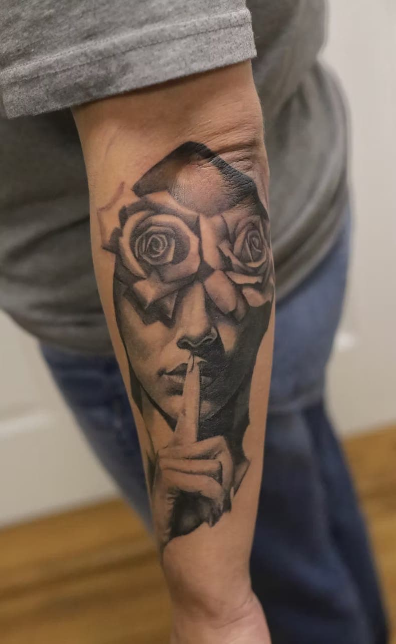 Black-and-grey surreal tattoo of a woman's face with roses for eyes and a finger to her lips, on a forearm, by 5 Pound Gummy Tattoo Collective