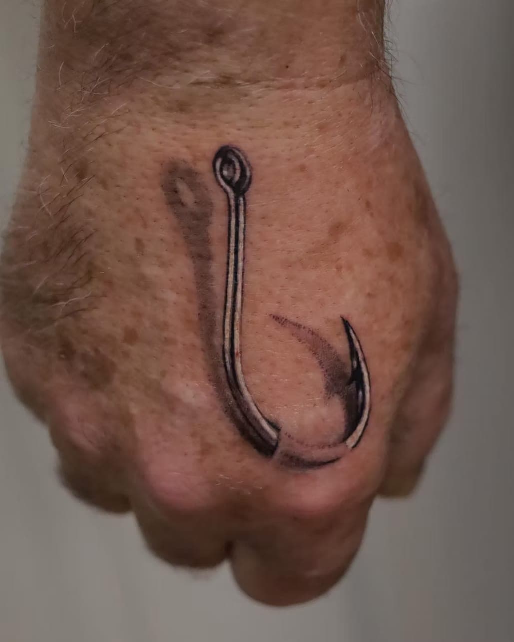 Black-and-grey realism tattoo of a fishing hook on the back of a hand by 5 Pound Gummy Tattoo Collective