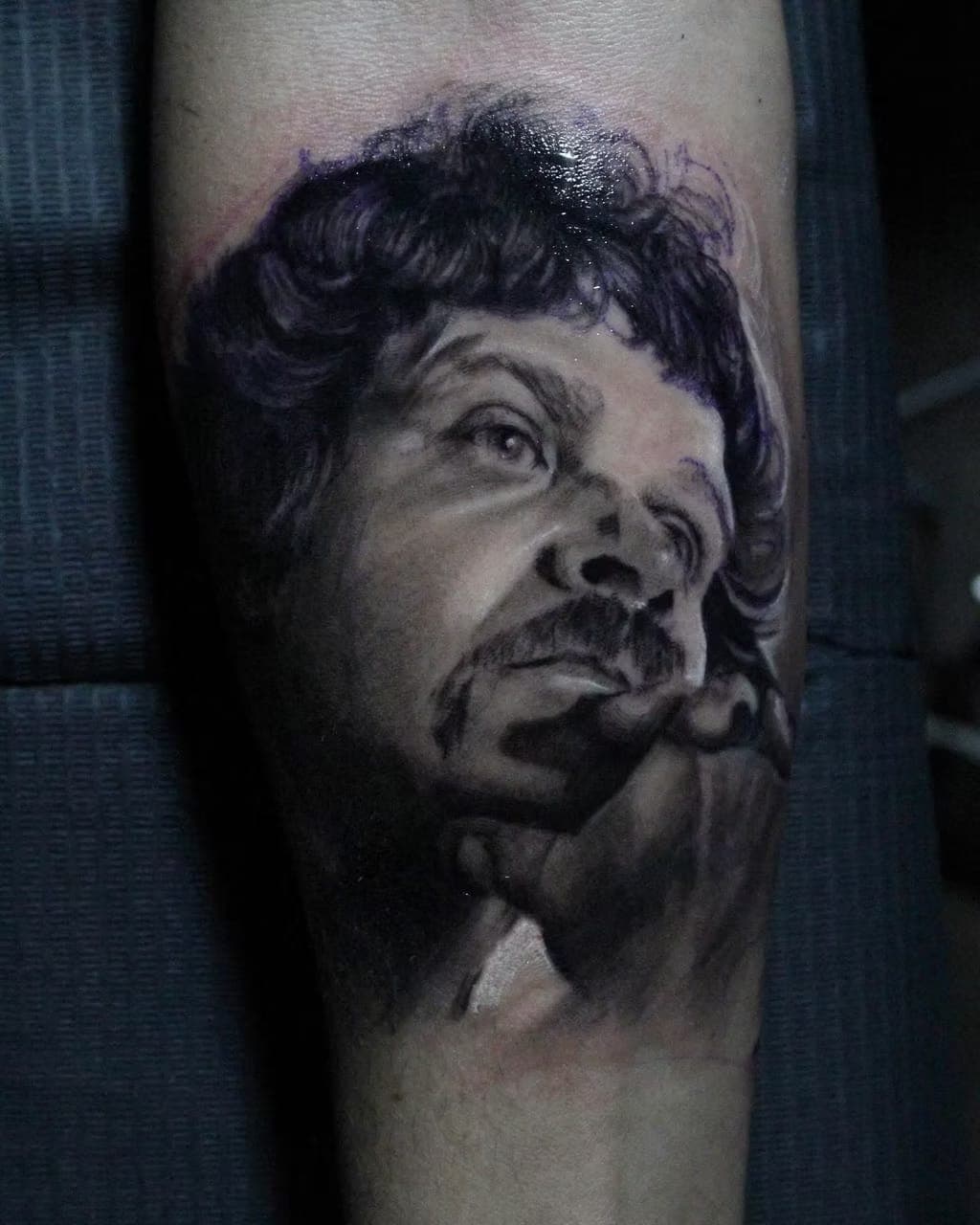 Black-and-grey realism portrait tattoo of a curly-haired man with a mustache by 5 Pound Gummy Tattoo Collective