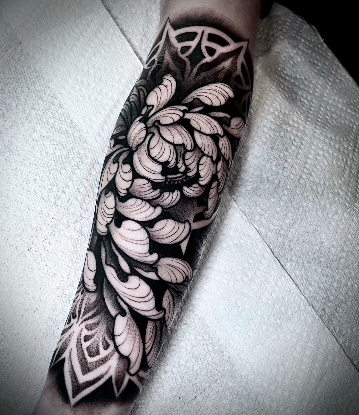 Black-and-grey floral forearm tattoo with mandala dotwork, by an artist at Capital Tattoo Company
