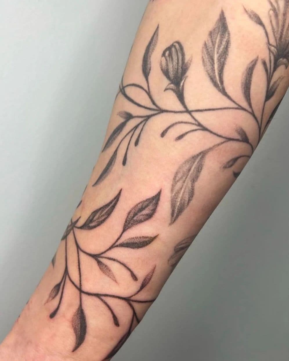 Fine-line botanical vine wrapped around a forearm, by an artist at Capital Tattoo Company