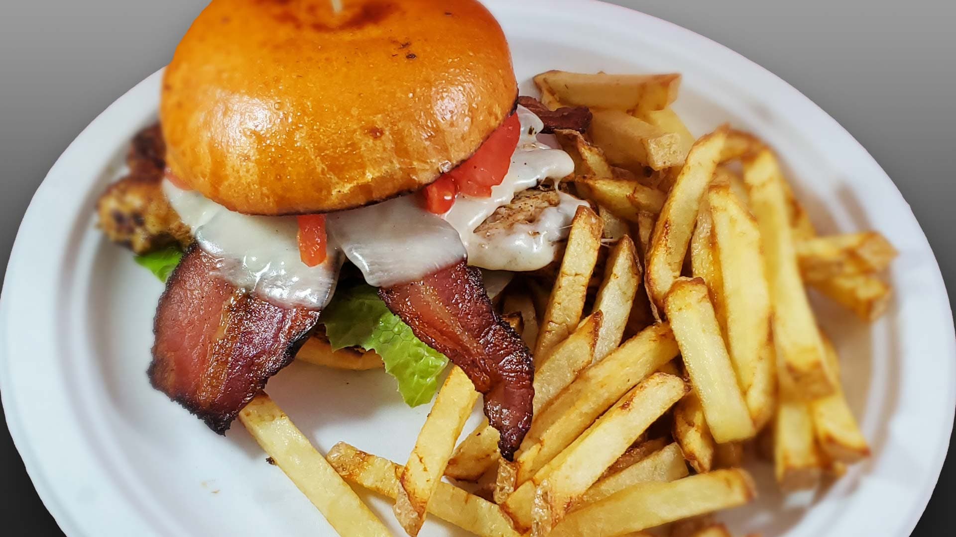 Bacon cheeseburger with melted cheese, lettuce, and tomato on a brioche bun, served with hand-cut fries at Cheezie Sam's Grill