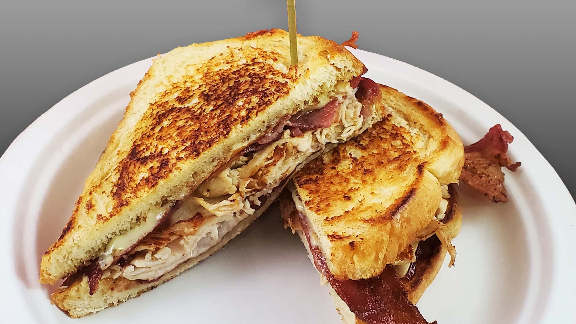 A gourmet grilled cheese melt on thick toasted bread, layered with chicken, bacon, and melted cheese and cut in half, at Cheezie Sam's Grill
