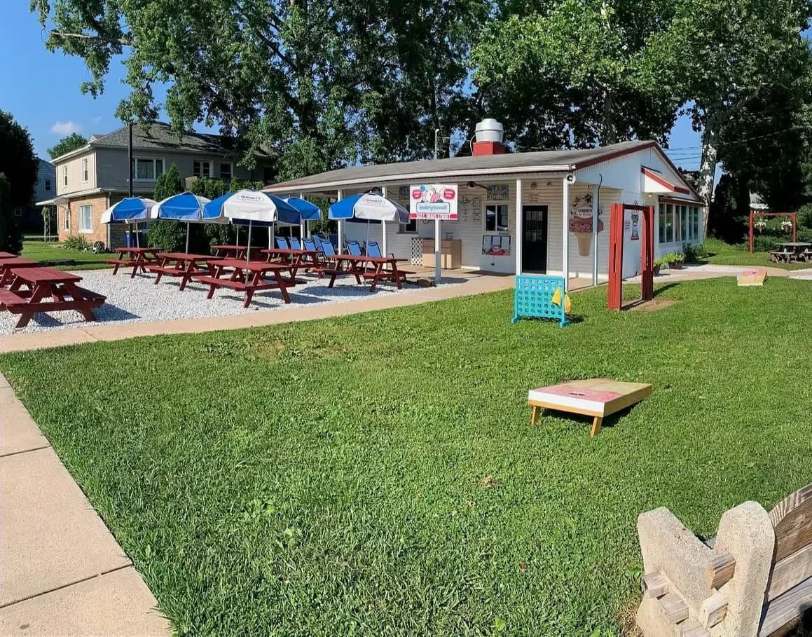 The Jak Frost Frozen Desserts ice cream shop in Middletown, PA, with picnic tables, colorful umbrellas, and a cornhole board on the lawn out front