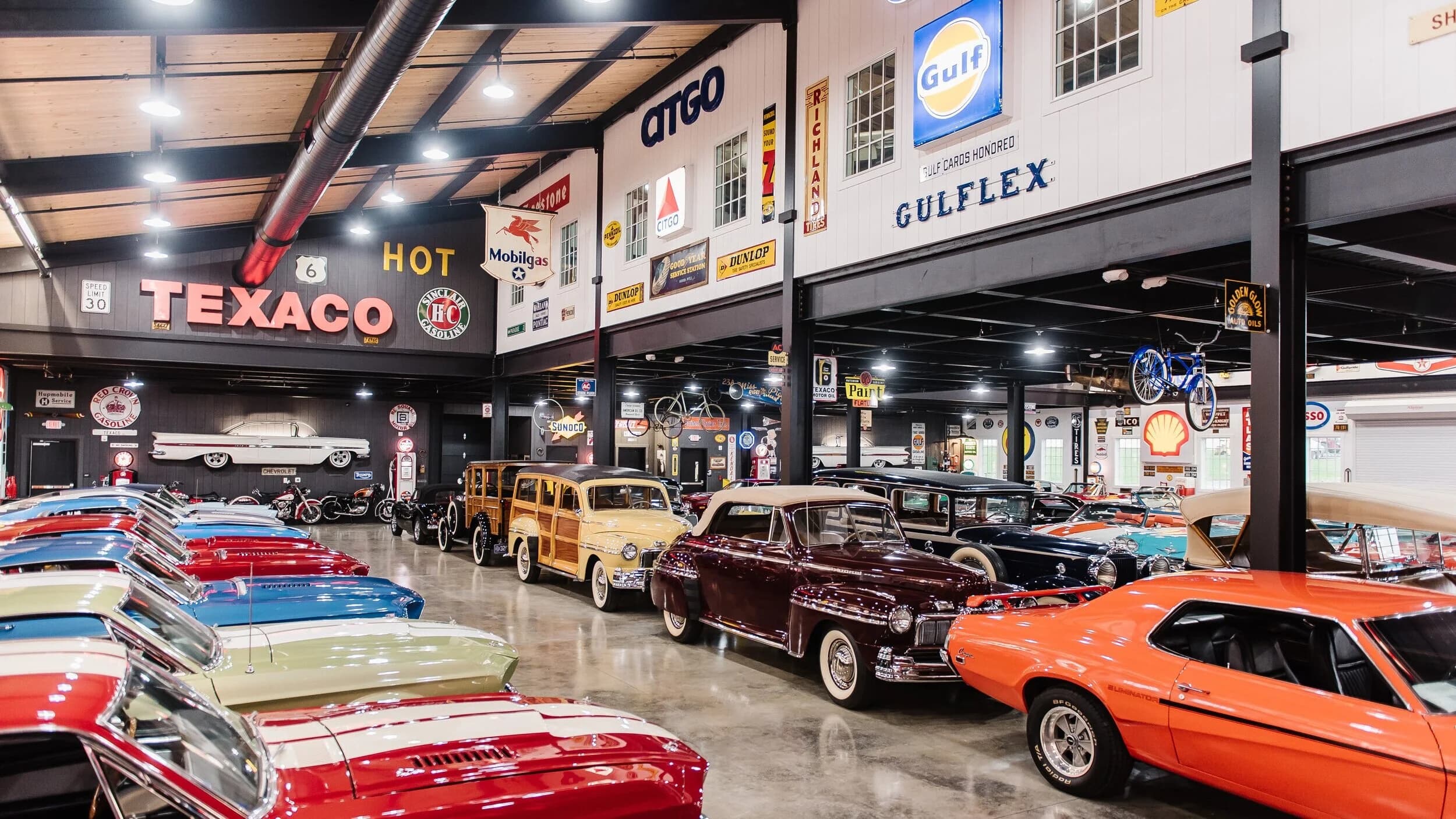 Rows of polished classic American cars inside Barry’s Car Barn, with vintage gas station signs and automotive displays on the walls.