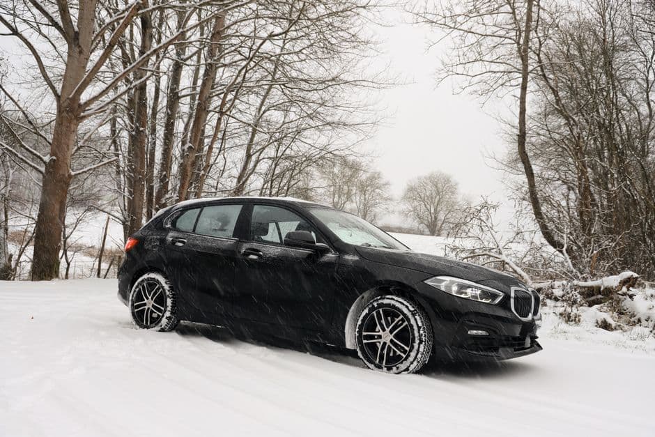 Black car driving through a snowy forest, showing winter tire considerations for Central PA drivers.