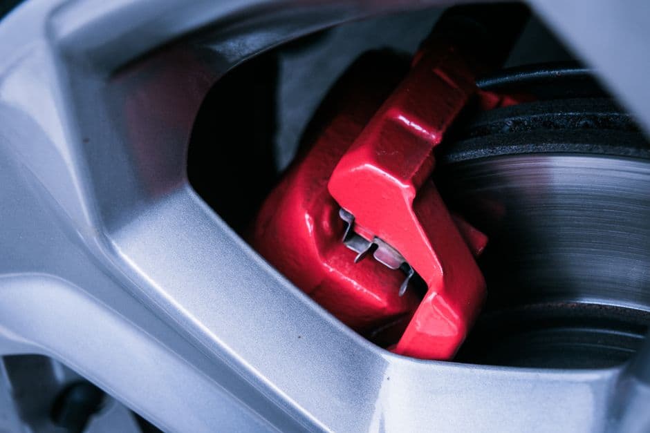 Detailed photo of a red automotive brake caliper and disc brake related to squeaky brakes.