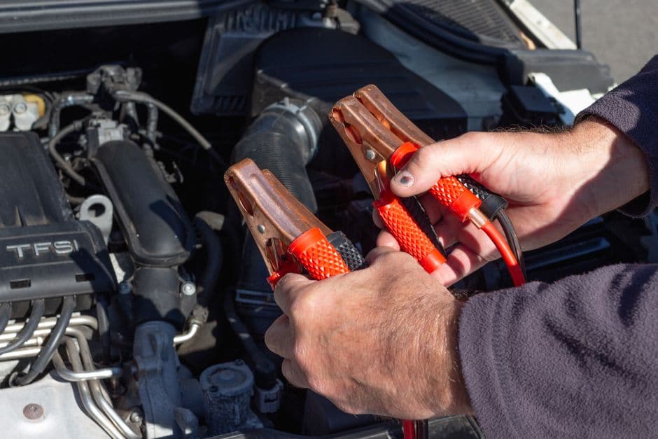 Close-up of hands holding jumper cables near a car engine for dead battery vs bad alternator diagnosis.