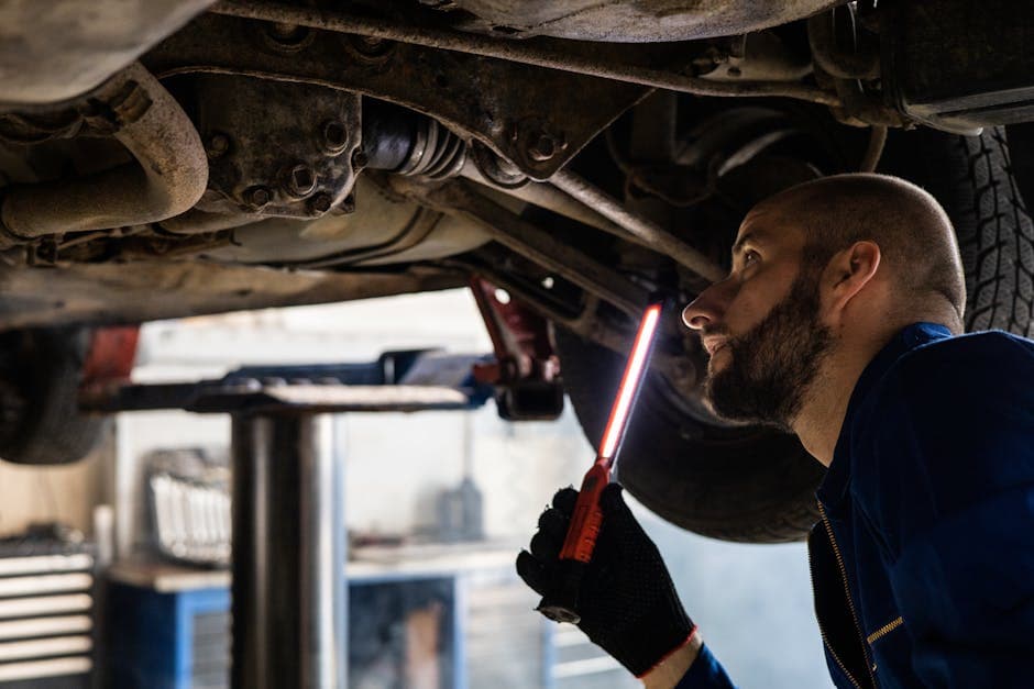Mechanic using a flashlight to inspect a vehicle undercarriage for a PA state inspection