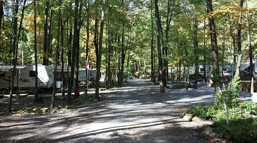 A wooded gravel lane lined with RVs and travel trailers under tall trees at Appalachian Campground in Shartlesville, PA, with an American flag flying