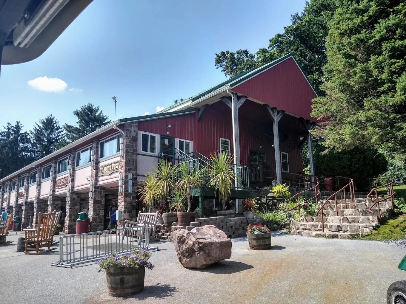 The red barn-style main lodge at Sun Retreats Lancaster County in Narvon, PA, with a stone base, rocking chairs, and potted plants out front